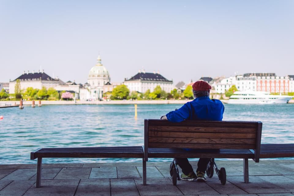 A man sits on a bench facing the water.