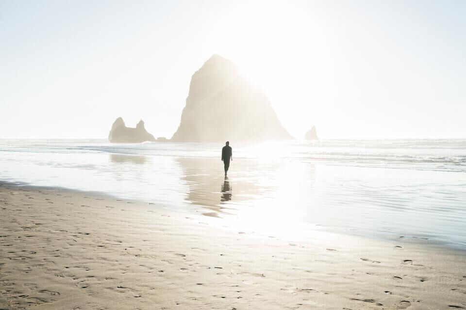 A man walks along a bright, empty beach toward the shore.